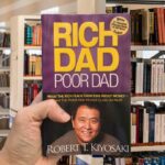 Cover of Rich Dad Poor Dad by Robert Kiyosaki, featuring a purple background, gold text, and a photo of the author.