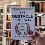 Cover of the book The Obstacle Is the Way by Ryan Holiday, featuring bold gold lettering on a black background with a laurel wreath.