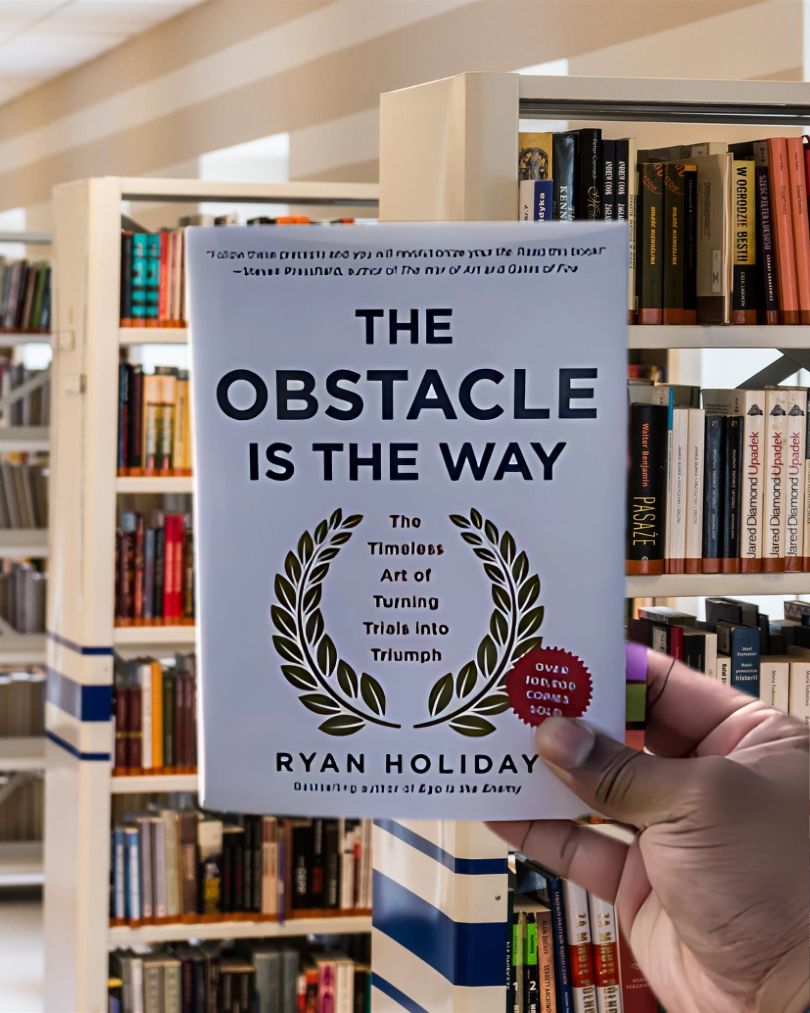 Cover of the book The Obstacle Is the Way by Ryan Holiday, featuring bold gold lettering on a black background with a laurel wreath.