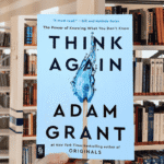 Book cover of Think Again by Adam Grant featuring a blue flame in the shape of a question mark on a white background.