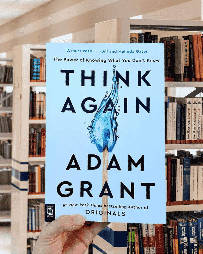 Book cover of Think Again by Adam Grant featuring a blue flame in the shape of a question mark on a white background.